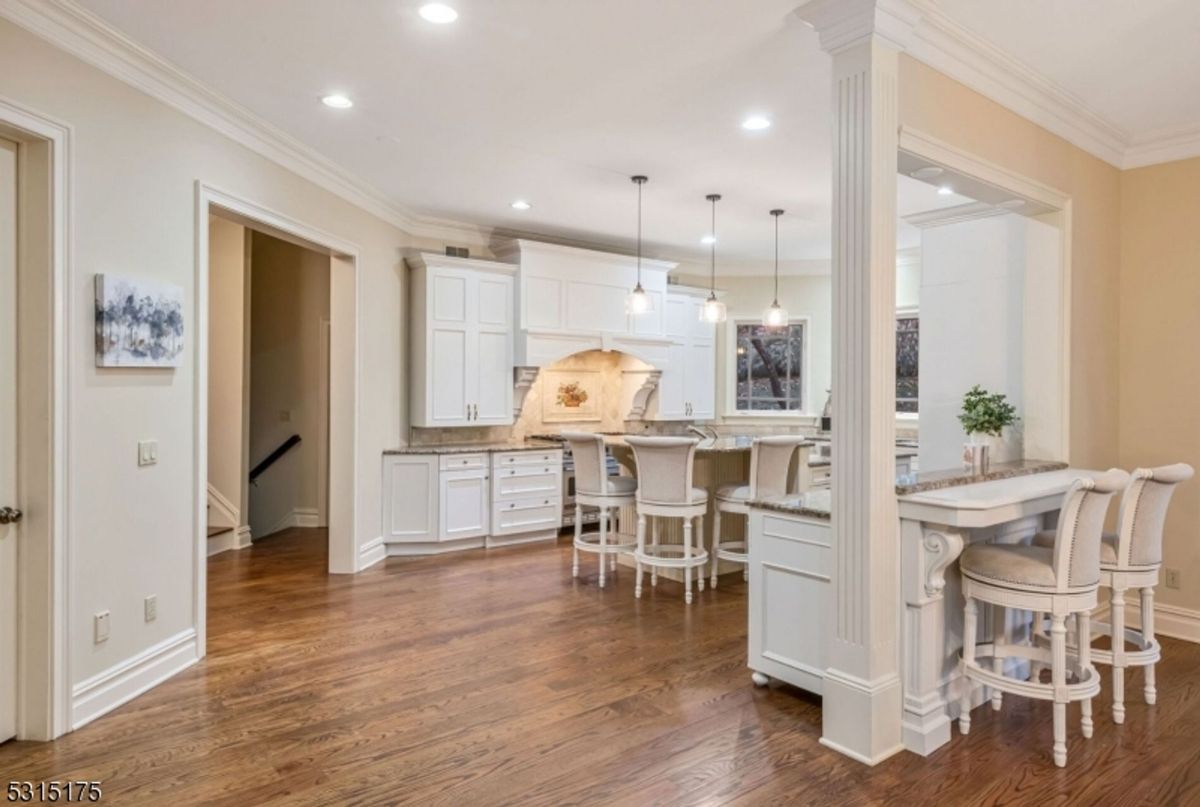 Bright kitchen layout features white cabinetry, an island with bar seating, and pendant lighting.