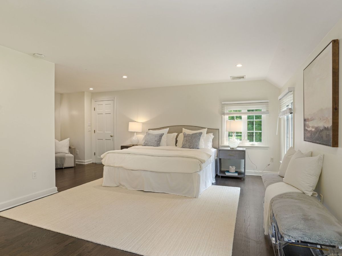 Bedroom with neutral tones, large windows, and cozy seating.