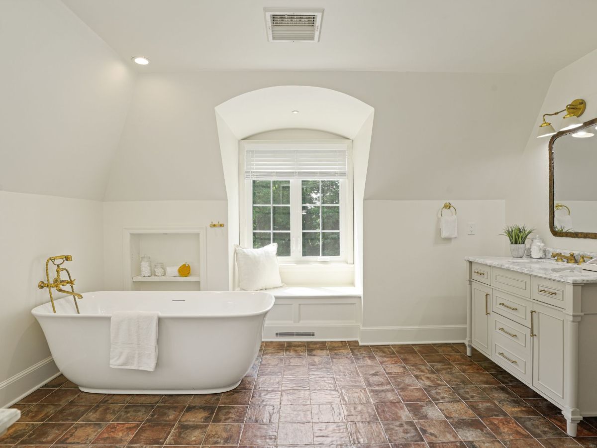 Bathroom with a freestanding tub, built-in window seat, and marble vanity.