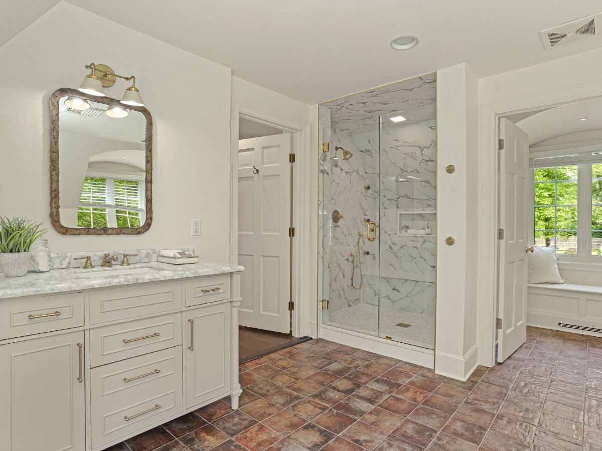 Refined bathroom with a marble shower, detailed vanity, and warm tile flooring.