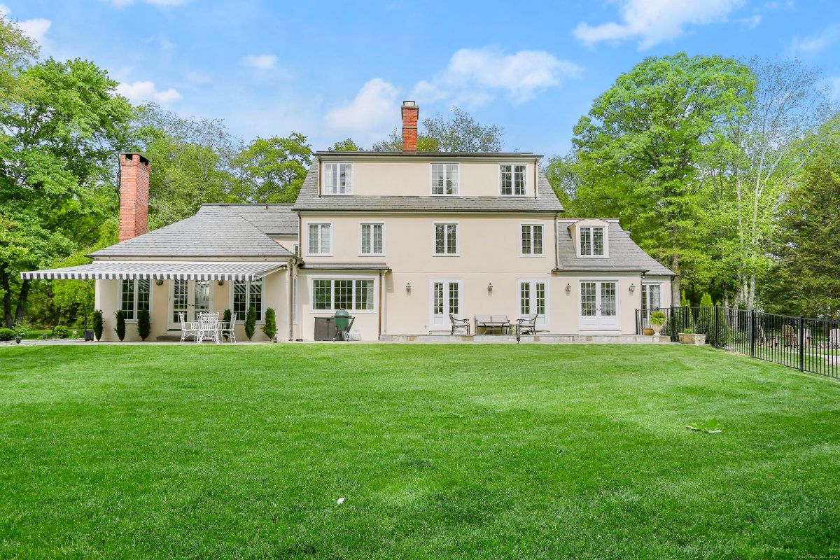 Charming estate with manicured lawn, striped awning, and elegant French doors.