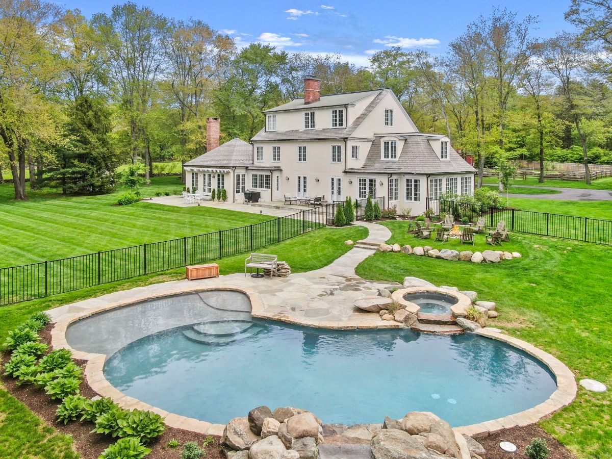 Expansive backyard with a custom pool, spa, and stone patio surrounded by lush landscaping.