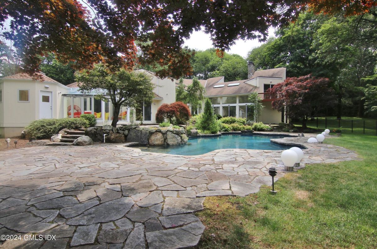 An expansive stone patio surrounds a sparkling freeform pool, complemented by lush landscaping and elegant outdoor lighting.