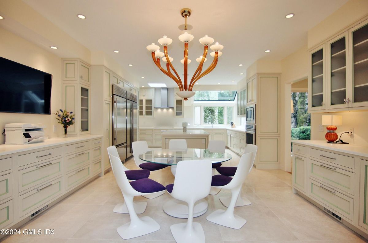 Gourmet kitchen showcases modern cabinetry, integrated appliances, and a glass dining table accented by a sculptural chandelier.