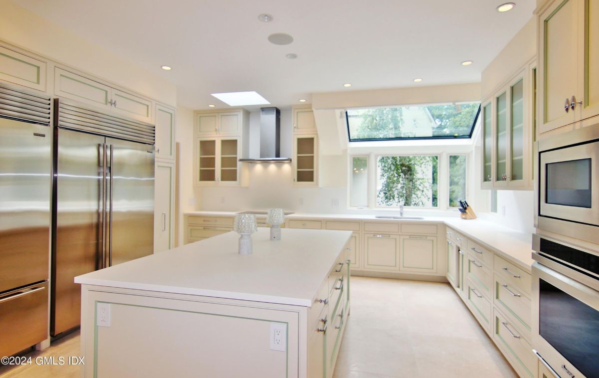 Kitchen highlights a central island, stainless steel appliances, and a skylight flooding the space with natural light.