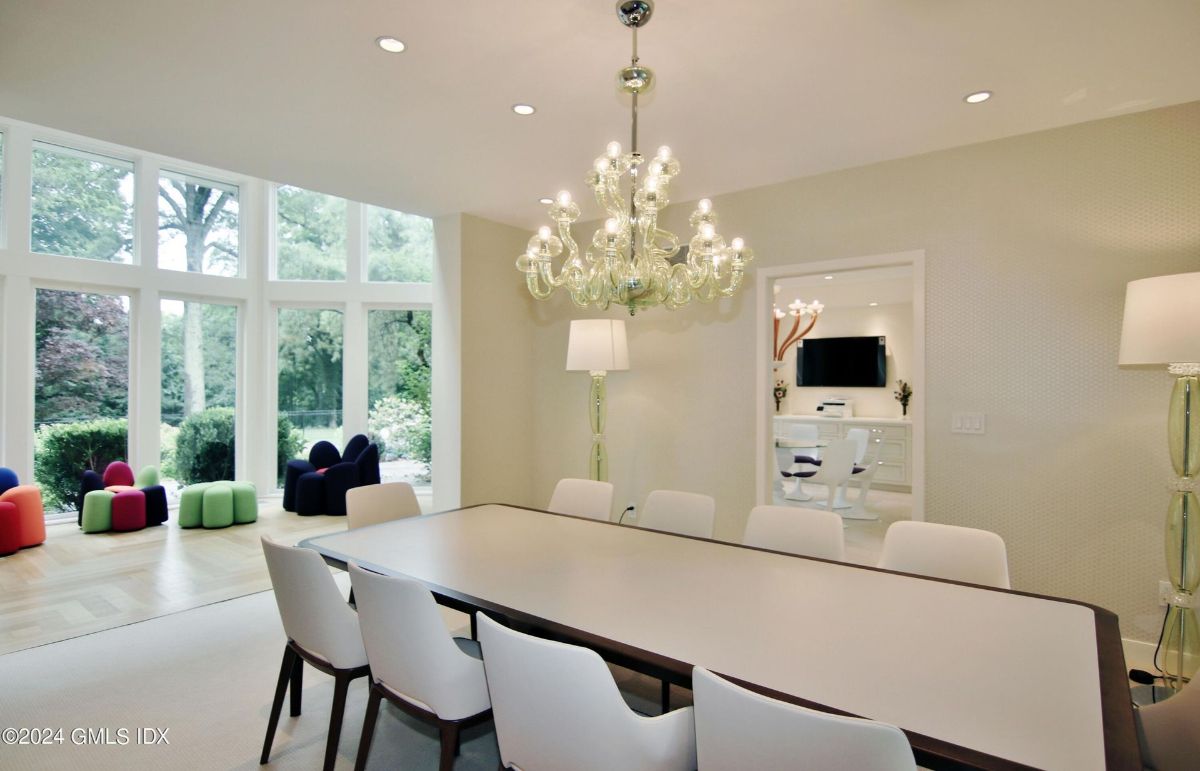 Elegant dining area is highlighted by a sparkling chandelier and surrounded by expansive windows overlooking lush greenery.