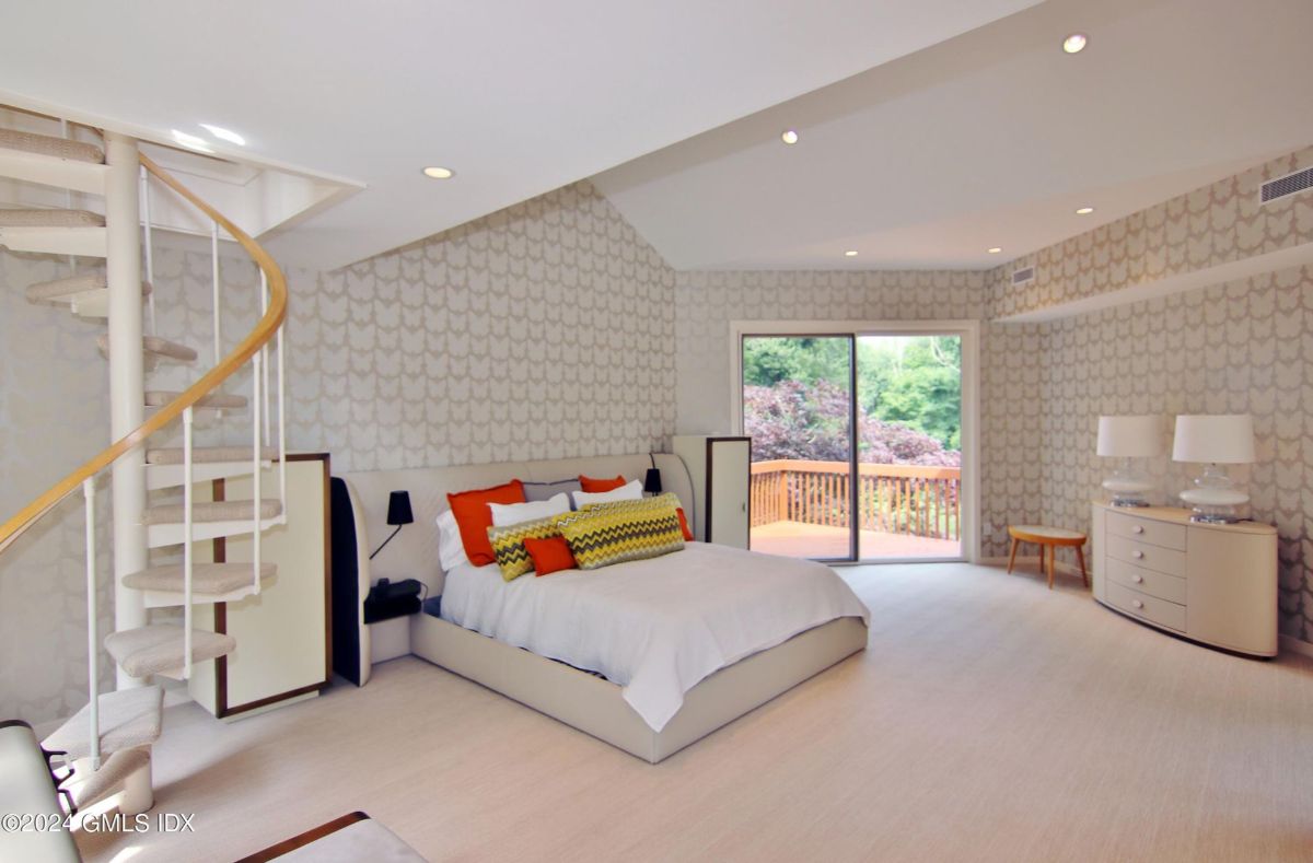 A chic bedroom showcases a spiral staircase and large sliding glass doors leading to a private balcony with scenic views.