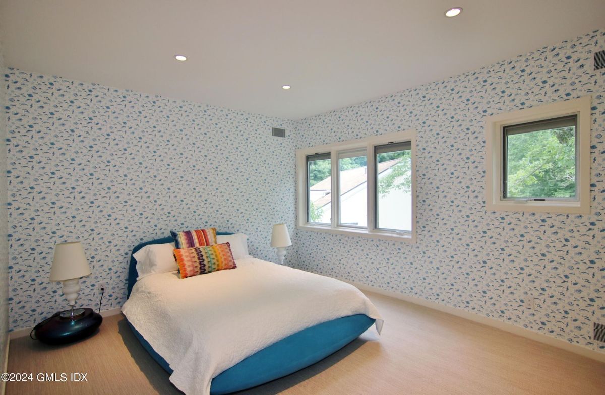 A cozy bedroom showcases whimsical wallpaper, a vibrant bedframe, and large windows offering serene views.