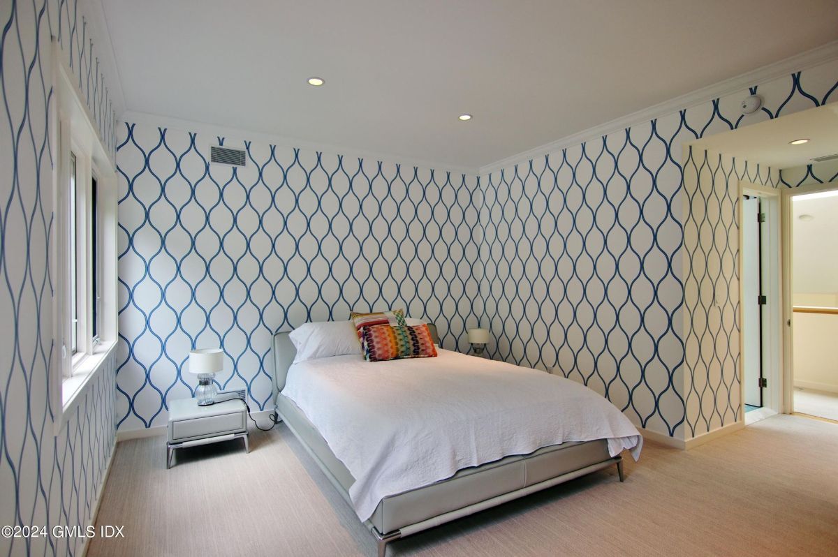 An elegant bedroom features bold geometric wallpaper, soft lighting, and a stylish bed for a modern aesthetic.