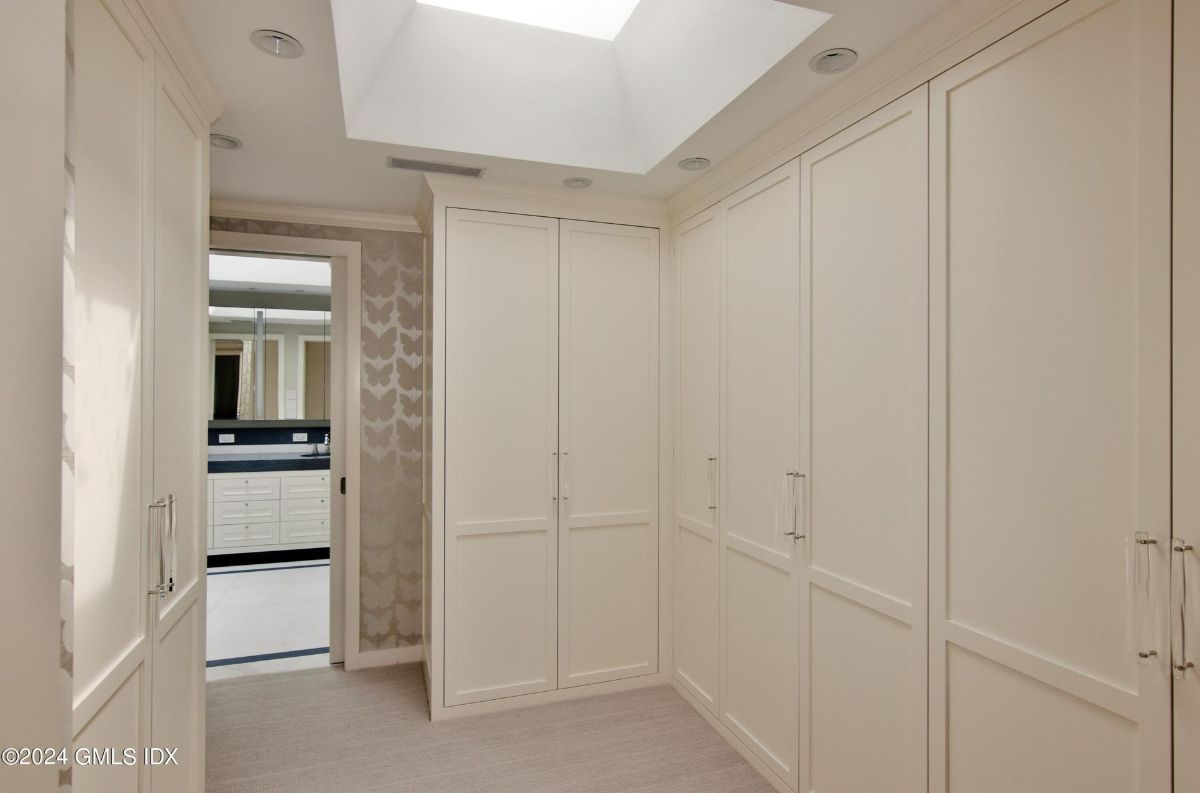 A skylit walk-in closet offers ample storage with sleek, custom cabinetry and seamless access to the master bathroom.