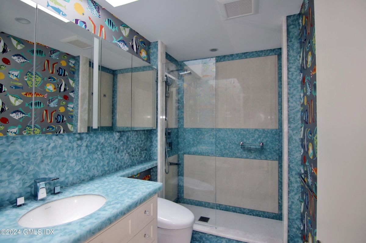 An aquatic-themed bathroom comes alive with vibrant fish-patterned walls, a textured blue countertop, and a modern glass-enclosed shower.