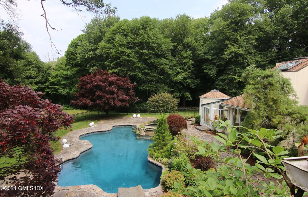 Backyard oasis features a beautifully landscaped pool area surrounded by vibrant foliage and mature trees.