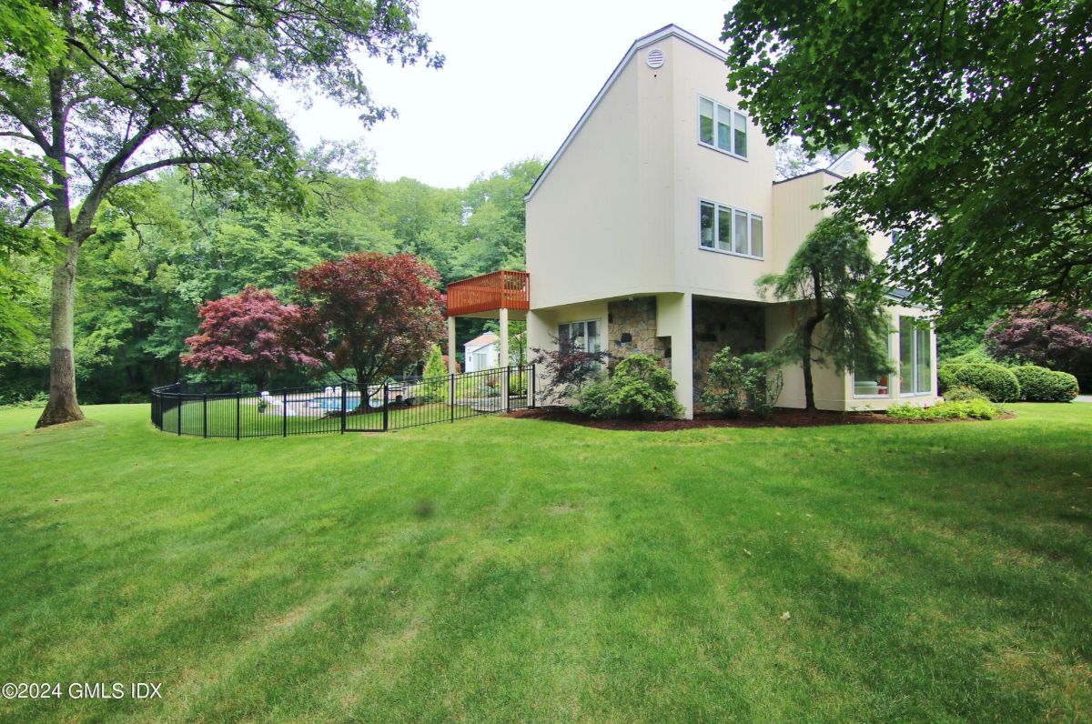 Expansive backyard blends lush greenery, mature trees, and a fenced-in pool area for serene outdoor living.