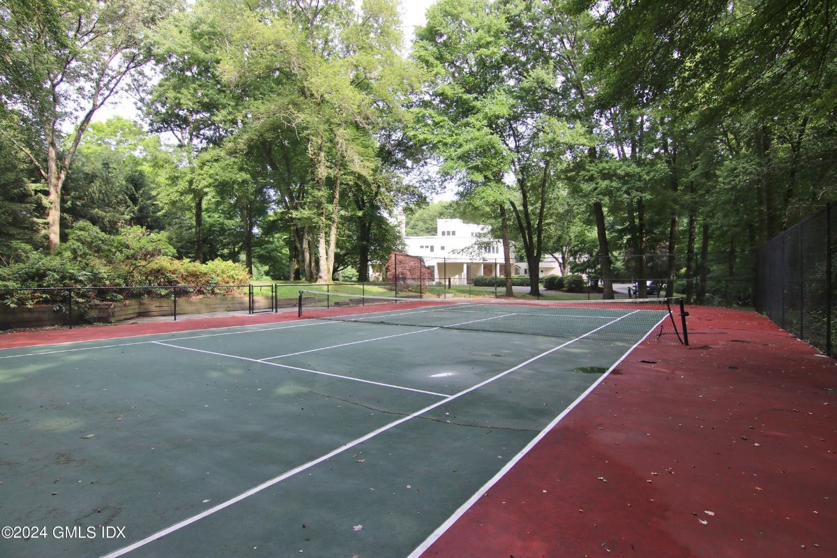 A private tennis court is nestled among mature trees, offering recreation in a serene setting.