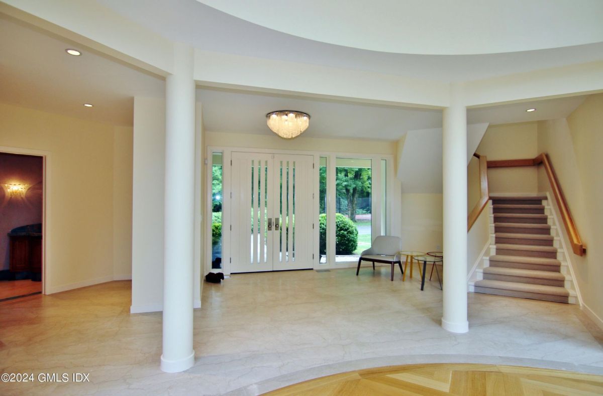 Curved columns and a chandelier add elegance to this spacious entryway, complemented by a staircase with warm wooden accents.