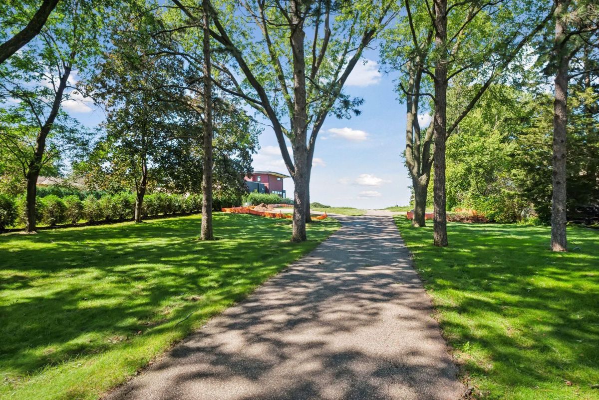 A tree-lined driveway leads to a serene property surrounded by lush greenery and open skies.