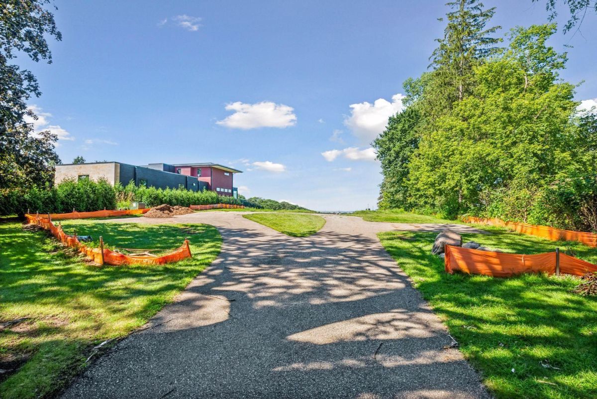 A winding driveway leads to a contemporary building surrounded by greenery.