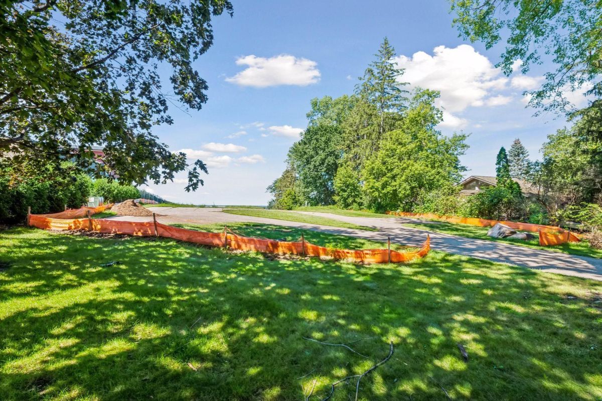 A shaded lawn frames a curving driveway lined with orange safety barriers.