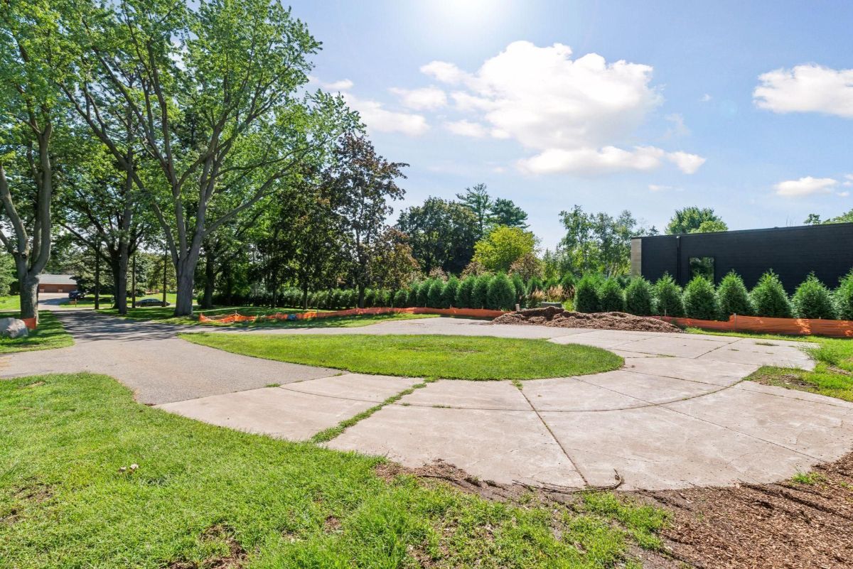 A circular driveway leads to a landscaped yard surrounded by lush trees and manicured shrubs.