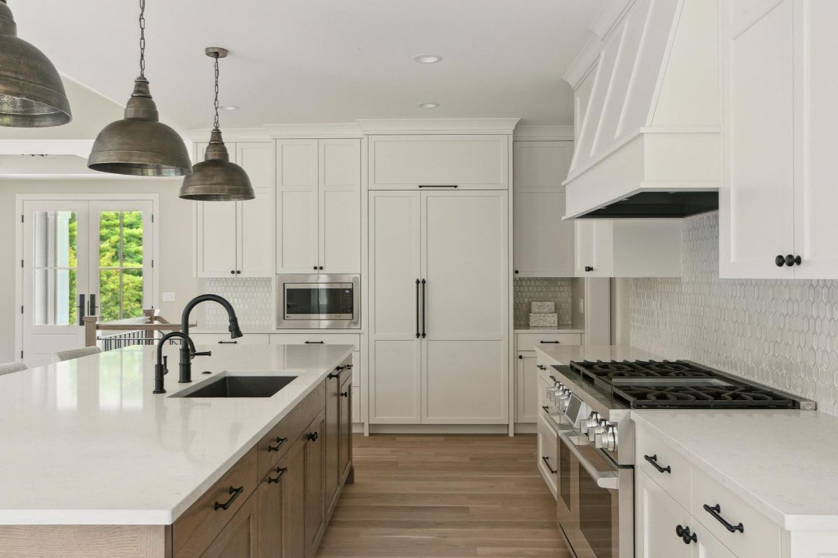 A bright kitchen features sleek cabinetry, a large island with a black sink, and pendant lights.