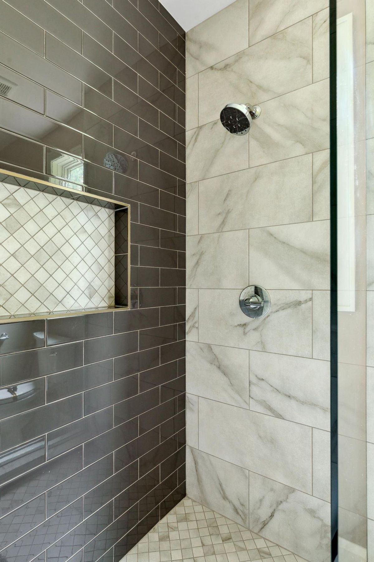 A luxurious shower features sleek dark tiles, a marble accent wall, and a built-in niche.