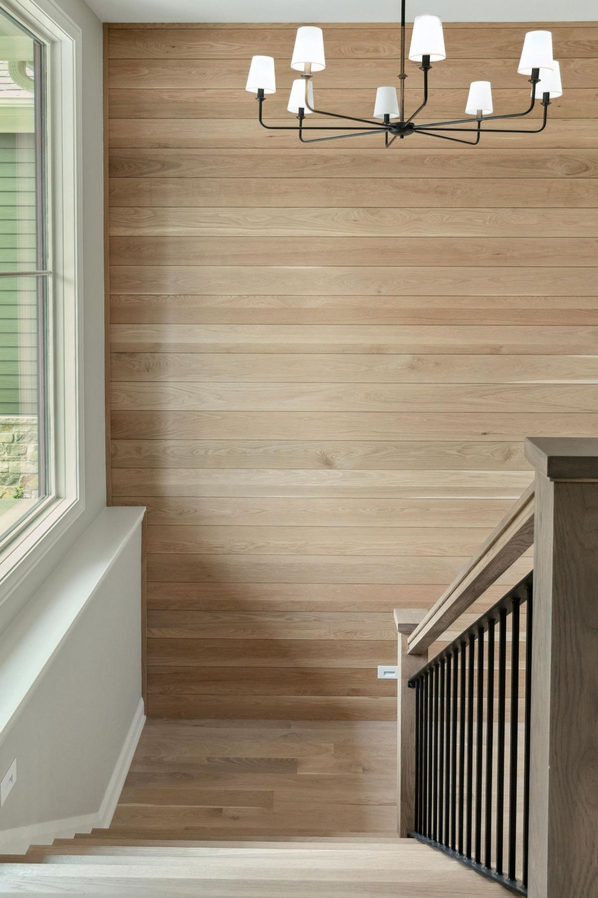 A staircase features natural wood accents, sleek black railing, and a modern chandelier.