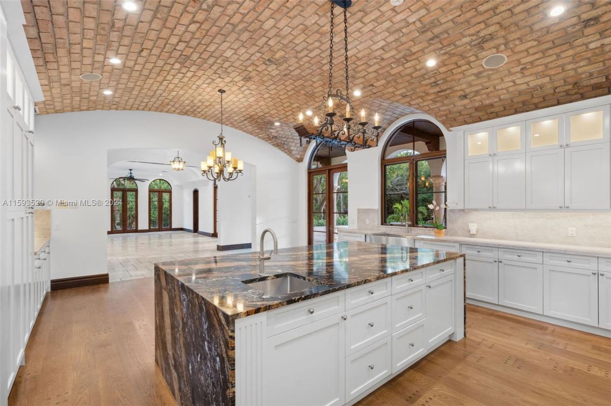 Stunning kitchen with a massive island featuring a marble countertop, arched brick ceiling, and elegant chandeliers illuminating the open layout.