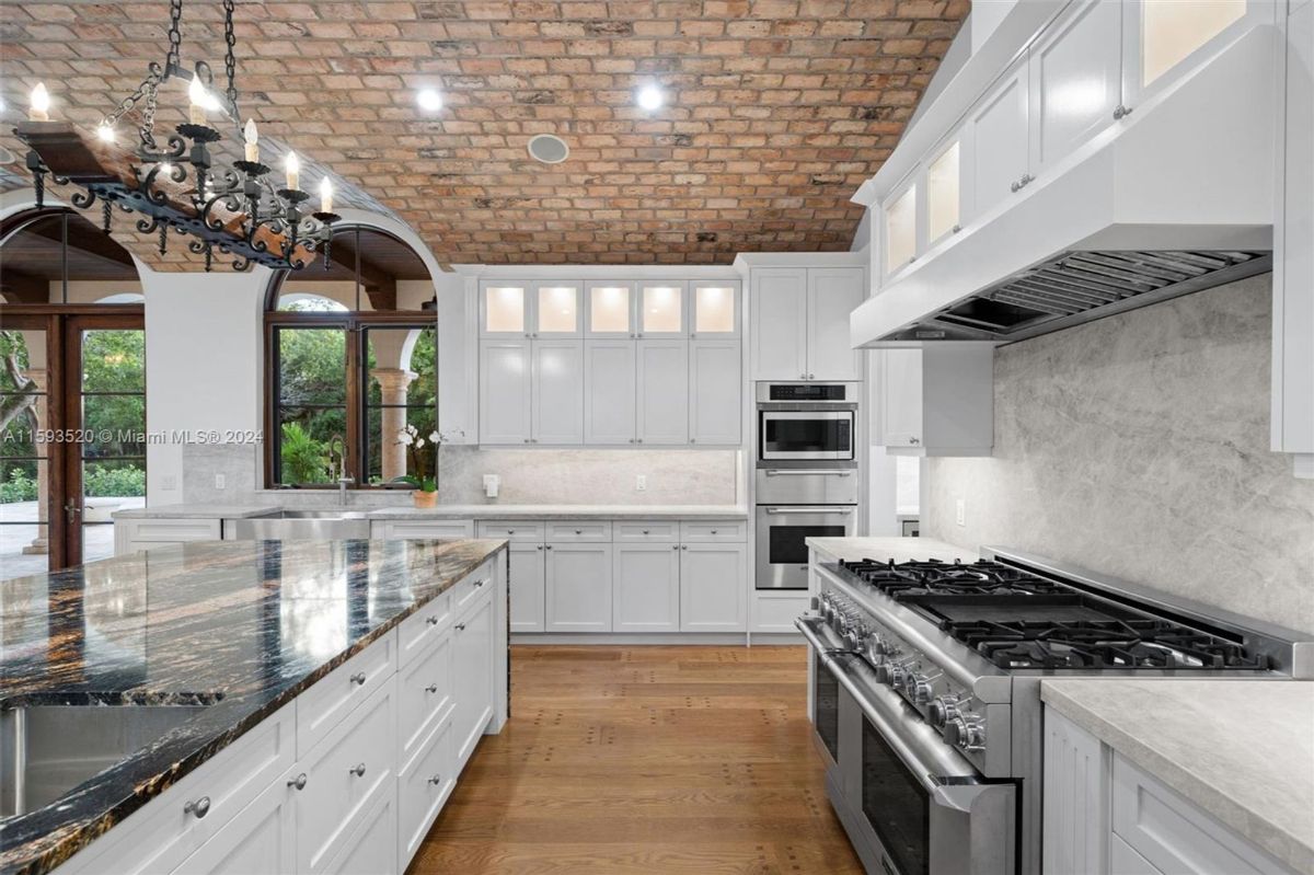 Gourmet kitchen equipped with a six-burner range, double ovens, sleek marble backsplash, and custom cabinetry under a vaulted brick ceiling.