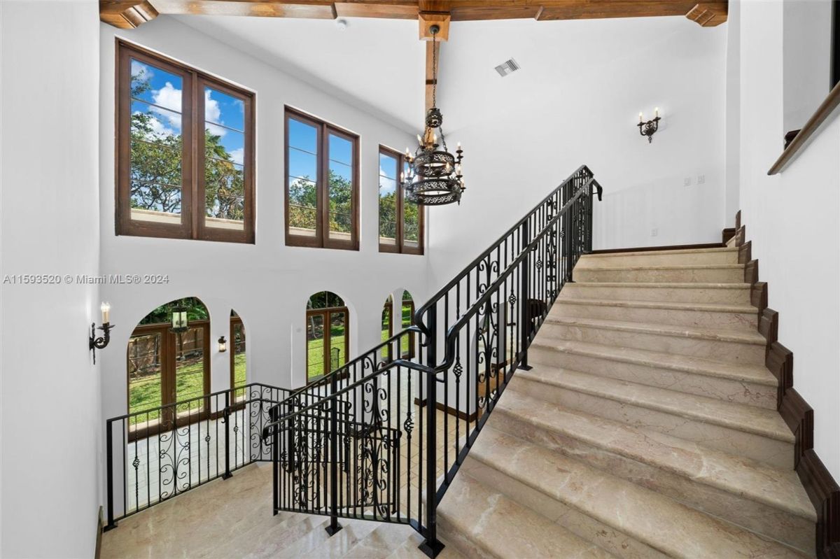 Marble staircase with ornate wrought-iron railing and large windows offering garden views.