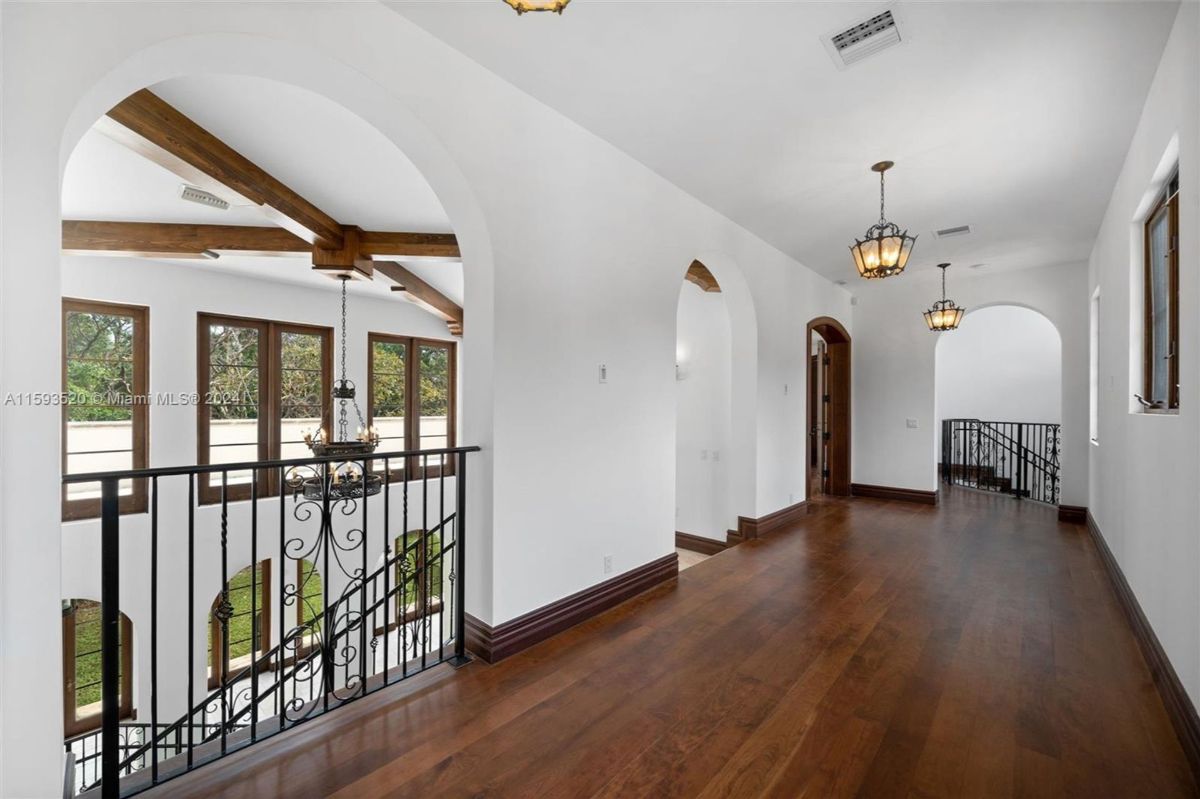 Upper hallway with rich hardwood flooring, arched doorways, and wrought iron railings overlooking the grand staircase.