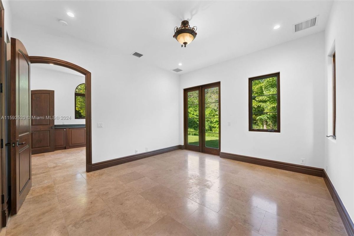 Bright room with polished stone floors, arched doorway, and large windows framing lush greenery.