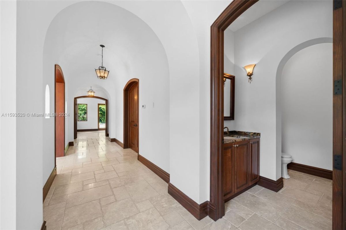 Hallway with arched ceilings, warm lighting, and a side powder room featuring a wood vanity and granite countertop.