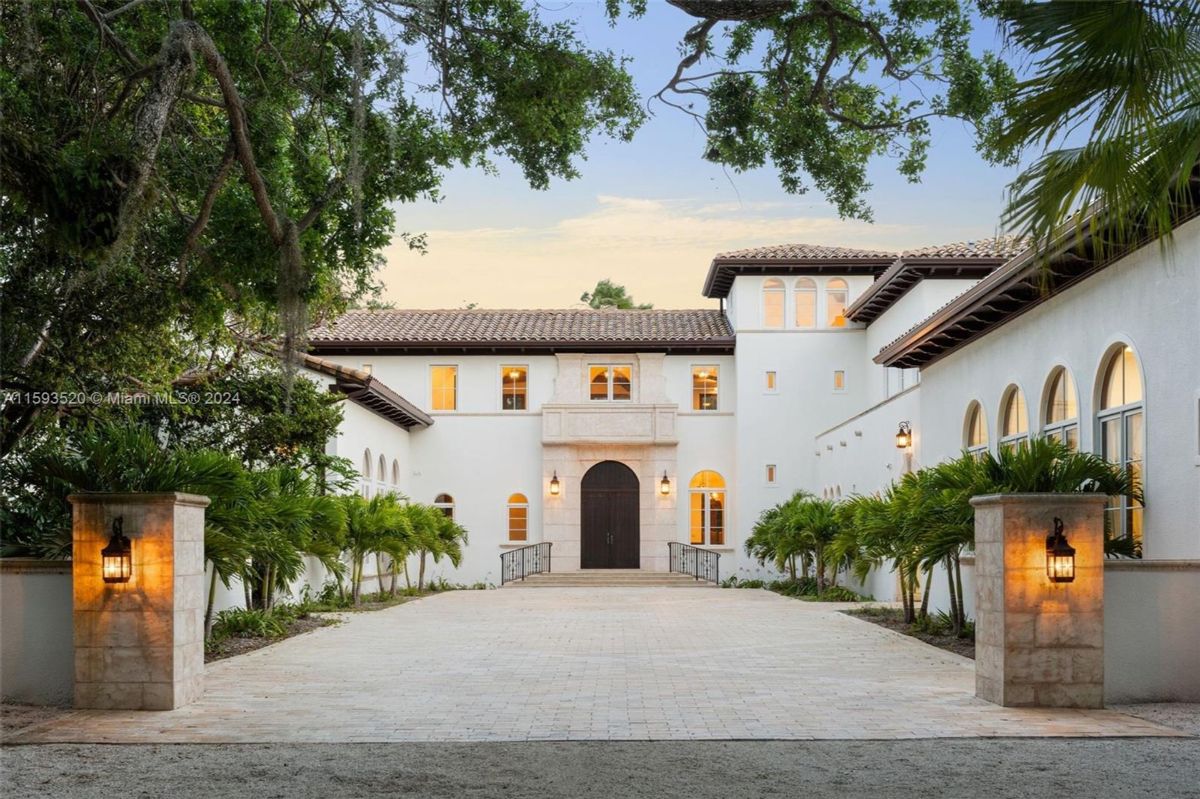 Elegant Mediterranean-style entrance framed by lush greenery and lantern-lit stone columns.