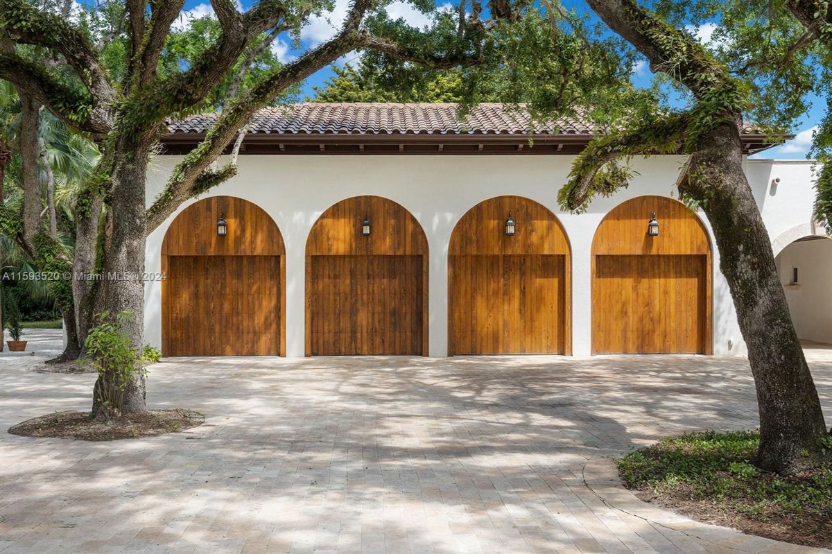 Four-car garage with wooden arched doors beneath mature oak trees.