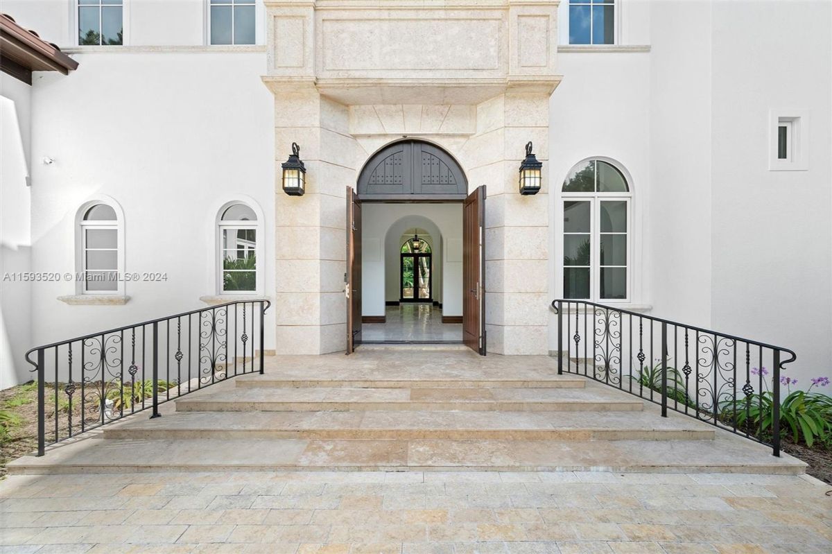 Grand stone entrance with arched double doors and wrought iron railing detailing.