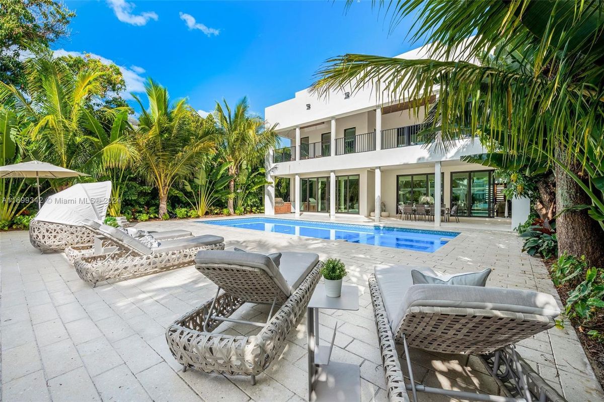 Tropical-inspired outdoor oasis featuring a pristine pool, spacious lounge area, and lush greenery enveloping a modern two-story villa.