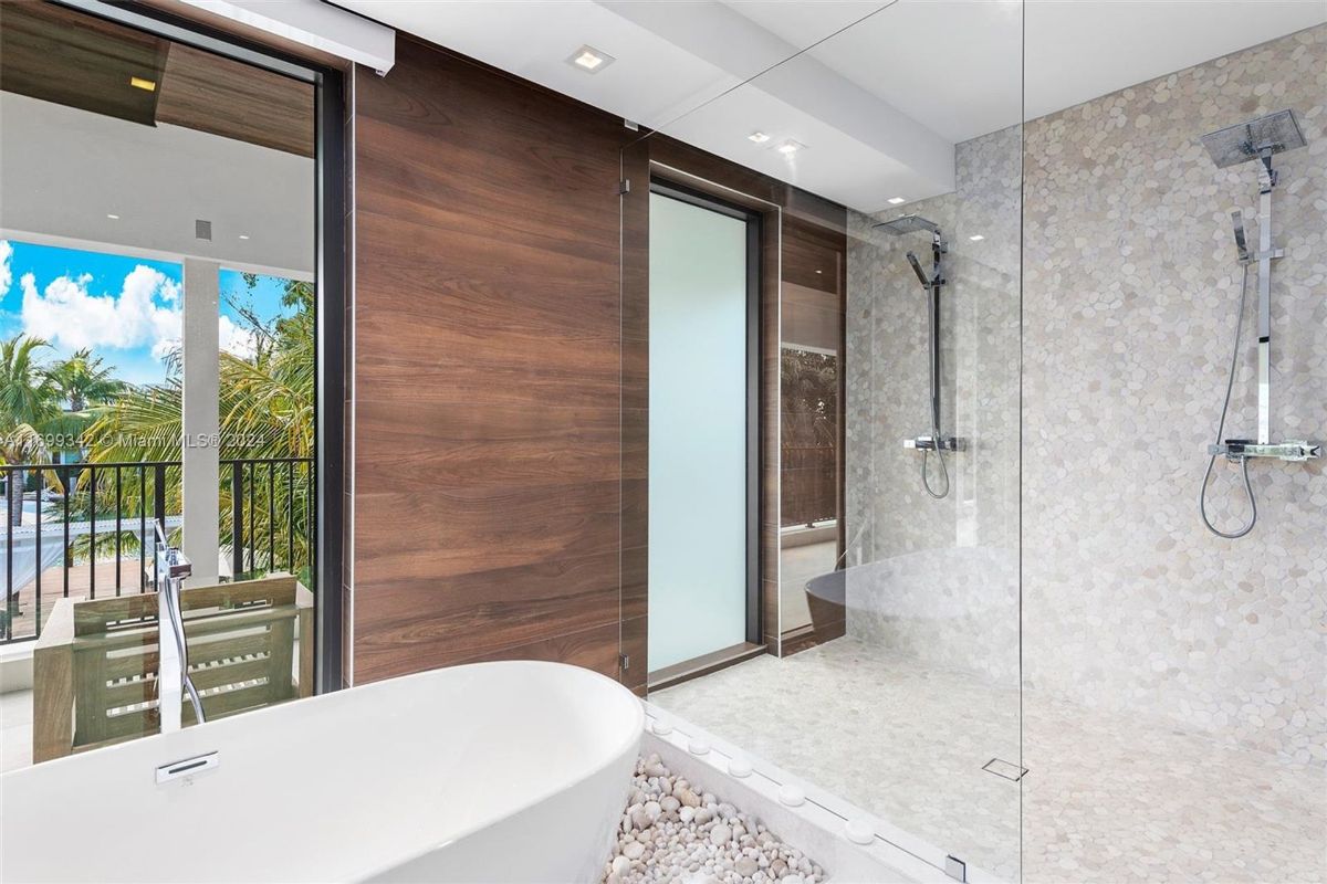 Spa-like bathroom with tub, pebble floor, and rain shower overlooking lush views.