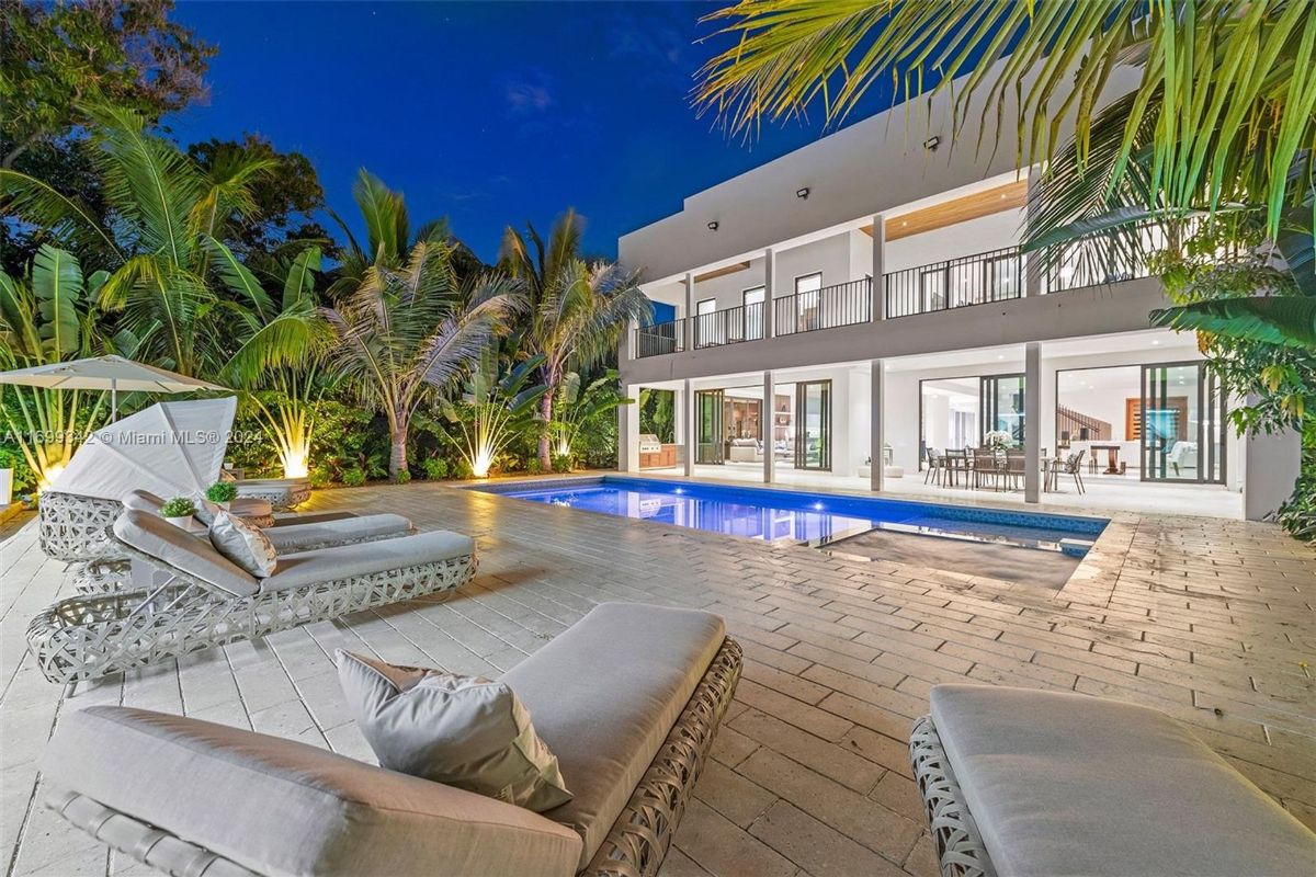 Tropical pool area illuminated by soft lighting, framed by lush greenery and modern architecture.