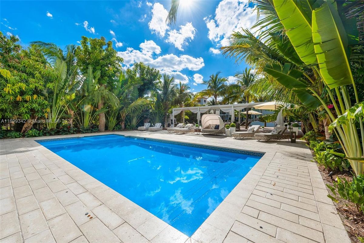 Pool bordered by vibrant tropical greenery and chic lounge spaces.