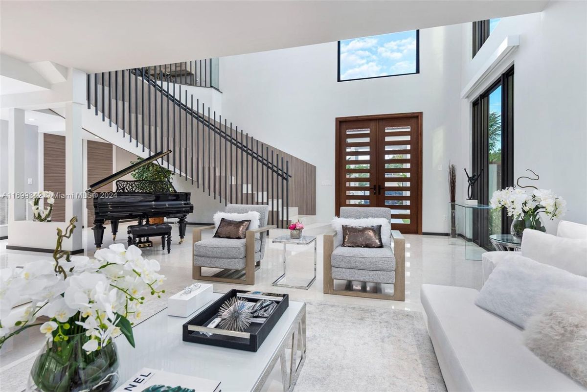 Living area with a grand piano, high ceilings, and a striking staircase.