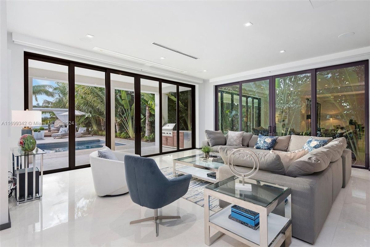 Family room with plush seating, glass walls opening to a poolside retreat, and abundant natural light.