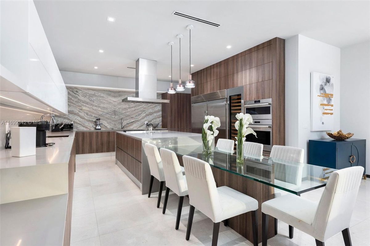 Gourmet kitchen showcasing wood-paneled cabinetry, marble backsplash, and a sleek glass dining table with modern lighting accents.