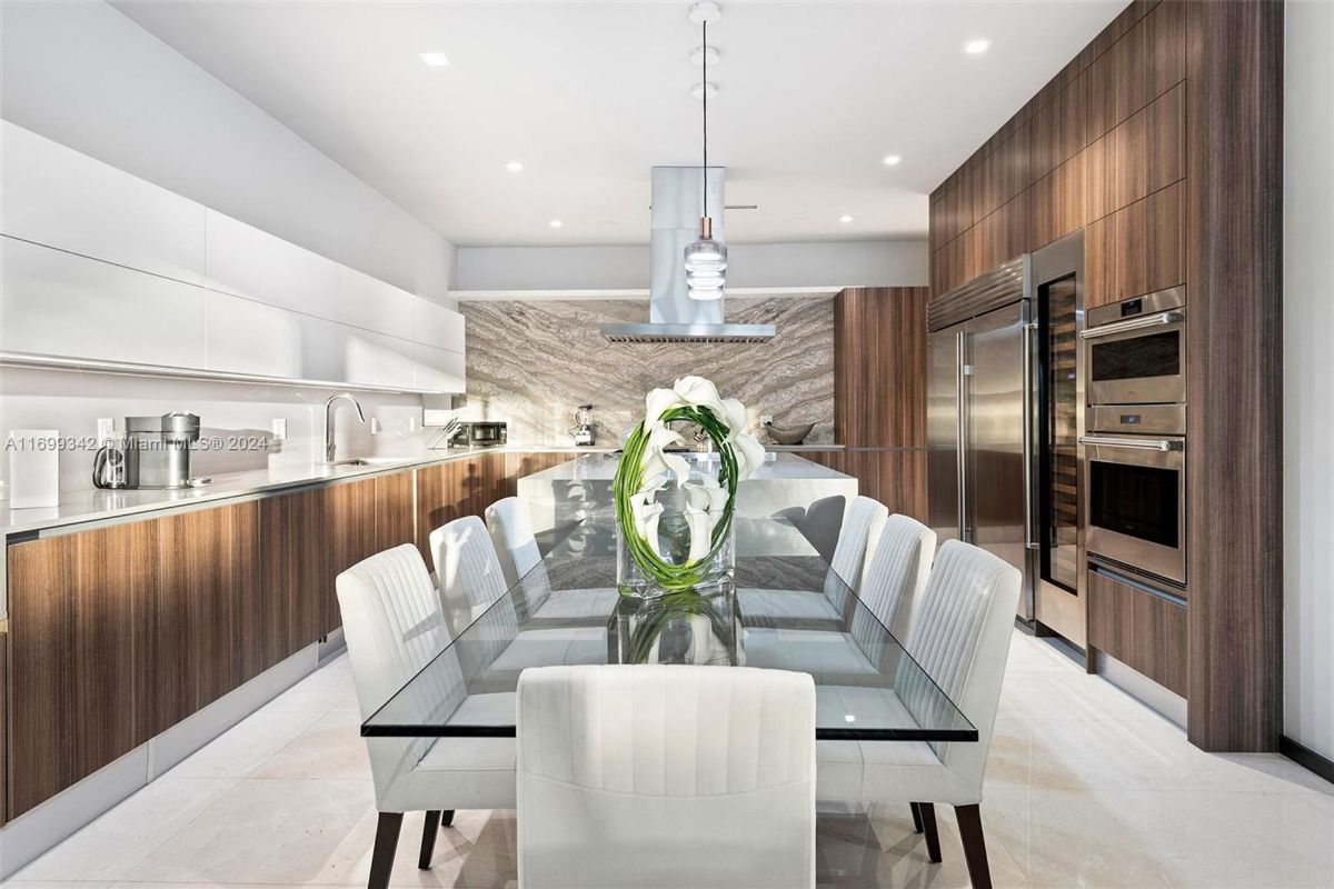 Sleek kitchen with high-gloss cabinetry, modern appliances, and a glass-top dining table under elegant pendant lighting.