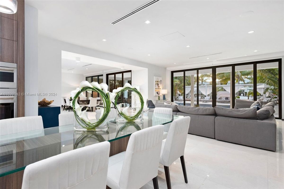 Dining and living area seamlessly blending indoor and outdoor spaces with expansive glass doors overlooking a tropical poolside retreat.