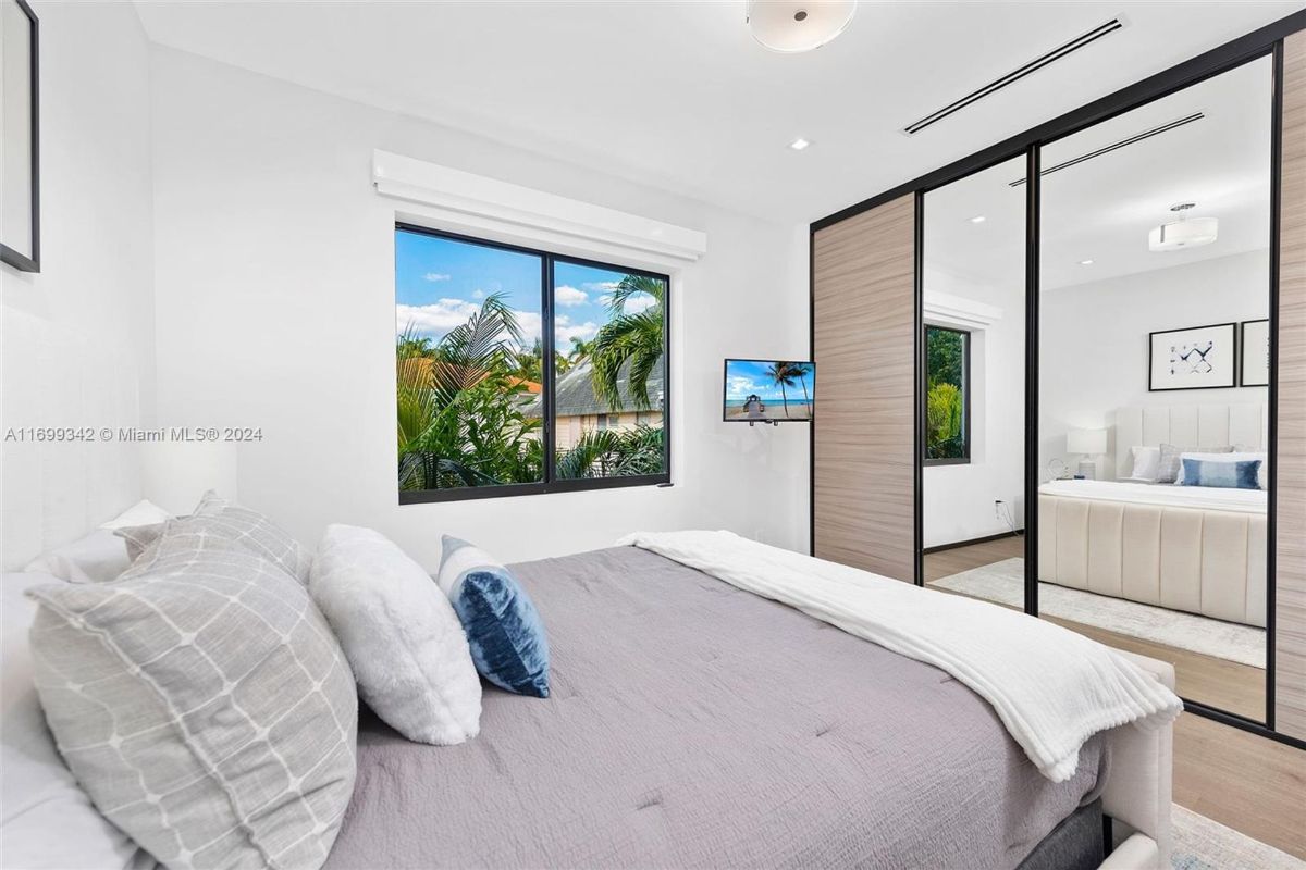 Natural light streams through large windows in the serene bedroom, featuring mirrored sliding doors and tropical garden views.