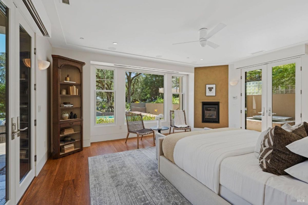 Elegant bedroom featuring large windows, a fireplace, and garden views.