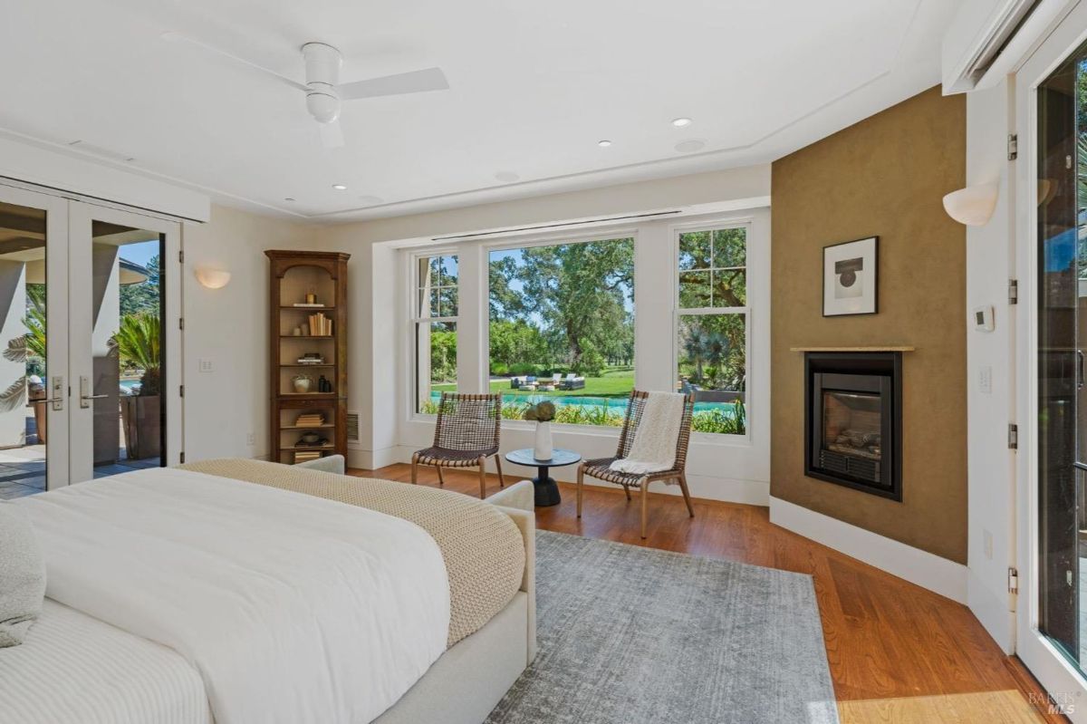 Bedroom with large windows, serene outdoor views, and a cozy fireplace for added ambiance.