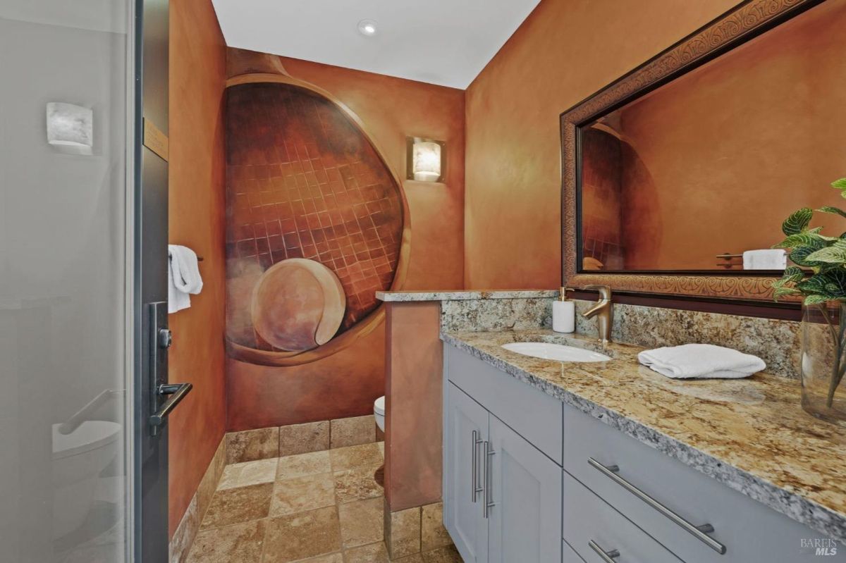 Stylish bathroom with a granite countertop, custom cabinetry, and a vibrant mural accent wall.