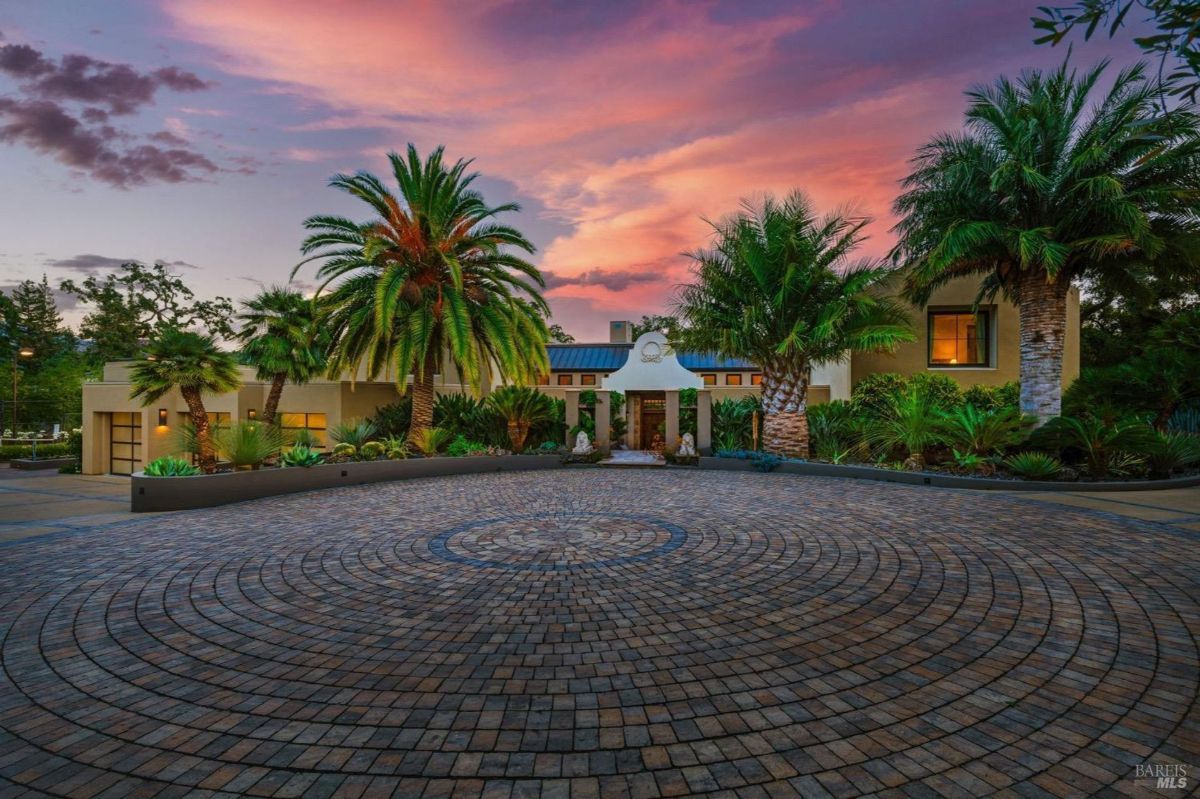 Circular driveway framed by palm trees, leading to a luxurious estate at sunset.