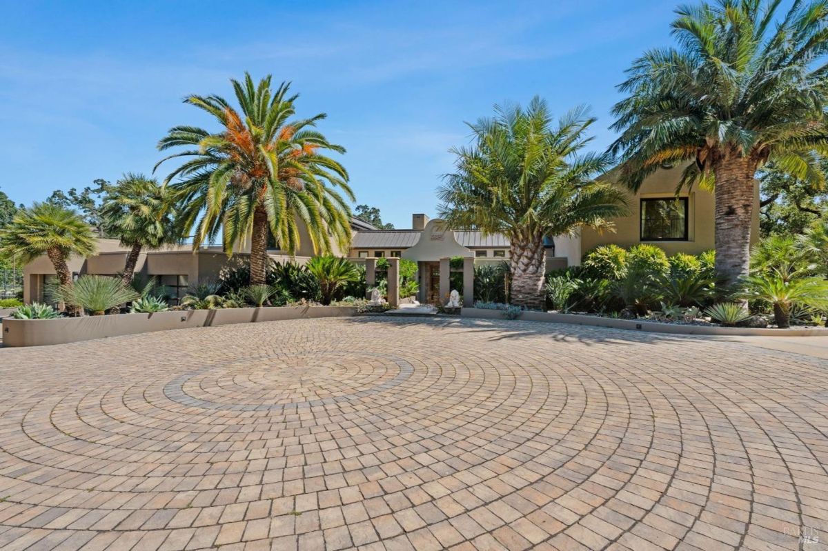 Expansive brick-paved driveway surrounded by lush palm trees and tropical landscaping.